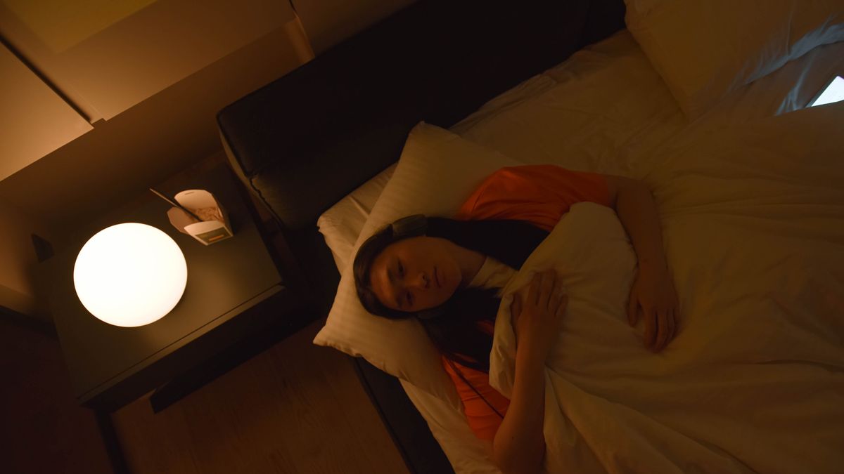 Overhead view of a woman lying awake in bed at night, lit by a bedside lamp