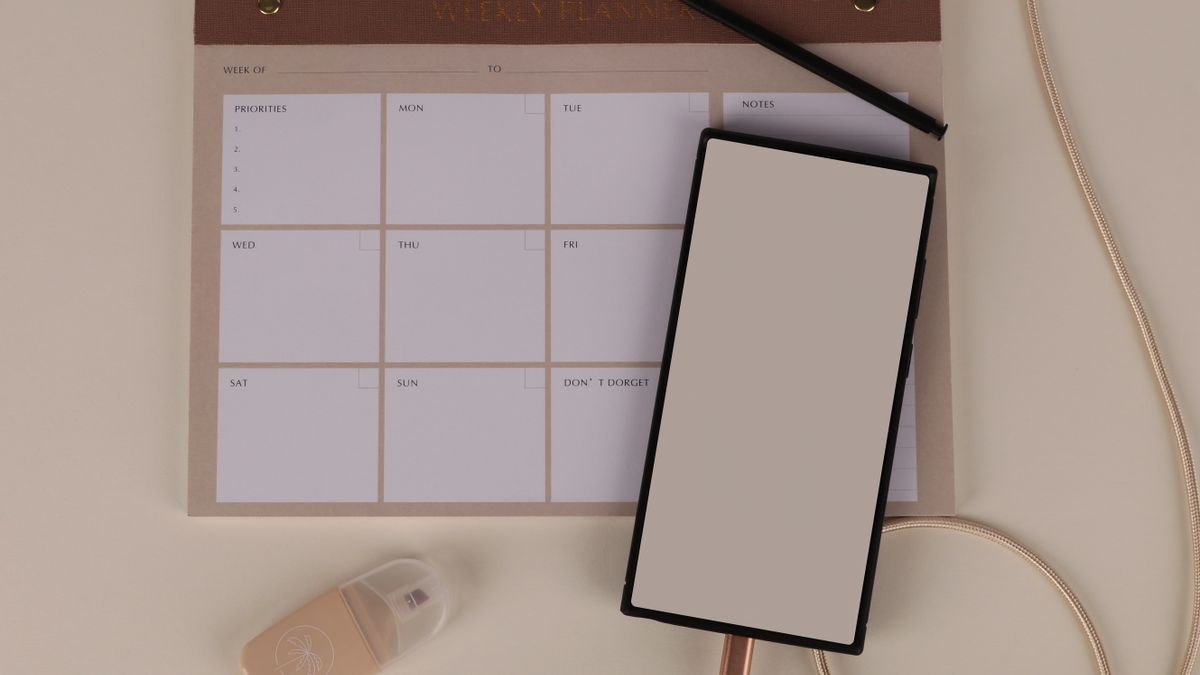 A weekly planner pad with priorities and days of the week beside a smartphone on a neutral desk